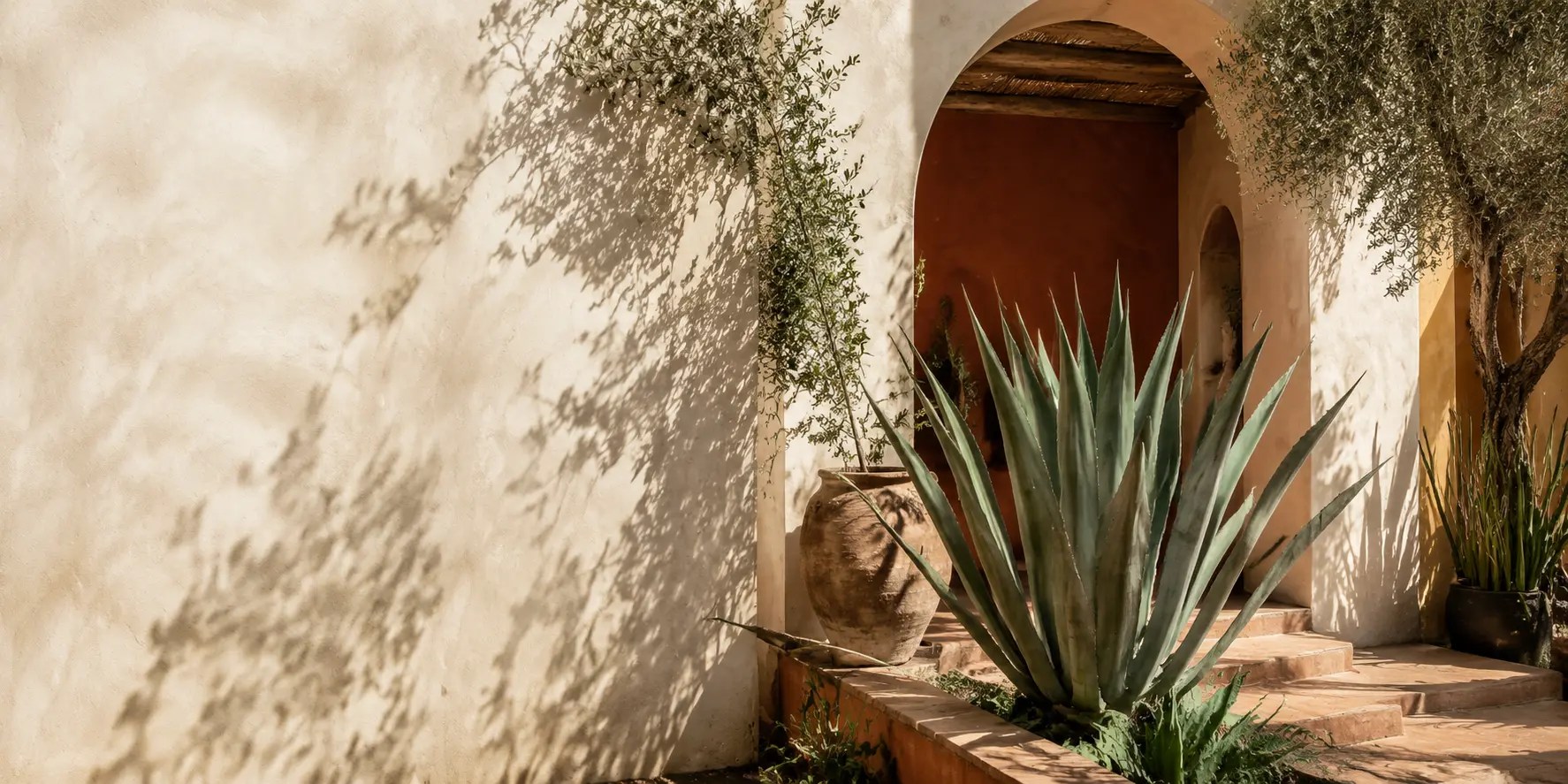 Patio méditerranéen lumineux avec une grande agave, des arches et des murs aux tons terre cuite.